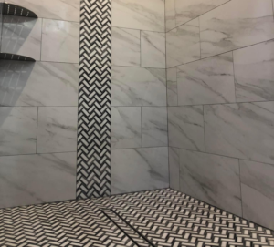 A walk in shower with a vertical accent strip going floor to ceiling about 12 inches wide. The field tile is a whit marble look porcelain and the accent strip is white and black mosaics. Along with the floor