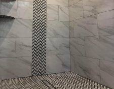 A walk in shower with a vertical accent strip going floor to ceiling about 12 inches wide. The field tile is a whit marble look porcelain and the accent strip is white and black mosaics. Along with the floor