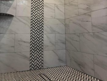 A walk in shower with a vertical accent strip going floor to ceiling about 12 inches wide. The field tile is a whit marble look porcelain and the accent strip is white and black mosaics. Along with the floor